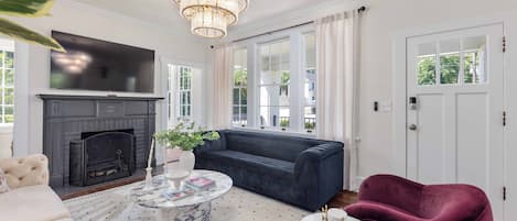 A living room with a fireplace, a large TV, a dark sofa, a round coffee table, and a red armchair.