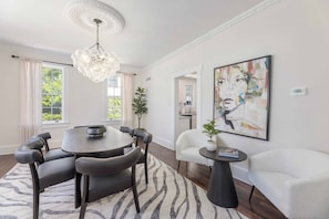 Ein Essbereich mit einem runden Tisch, Stühlen, einer Chandelierleuchte, einem zebra-gemusterten Teppich und einem Gemälde an der Wand.