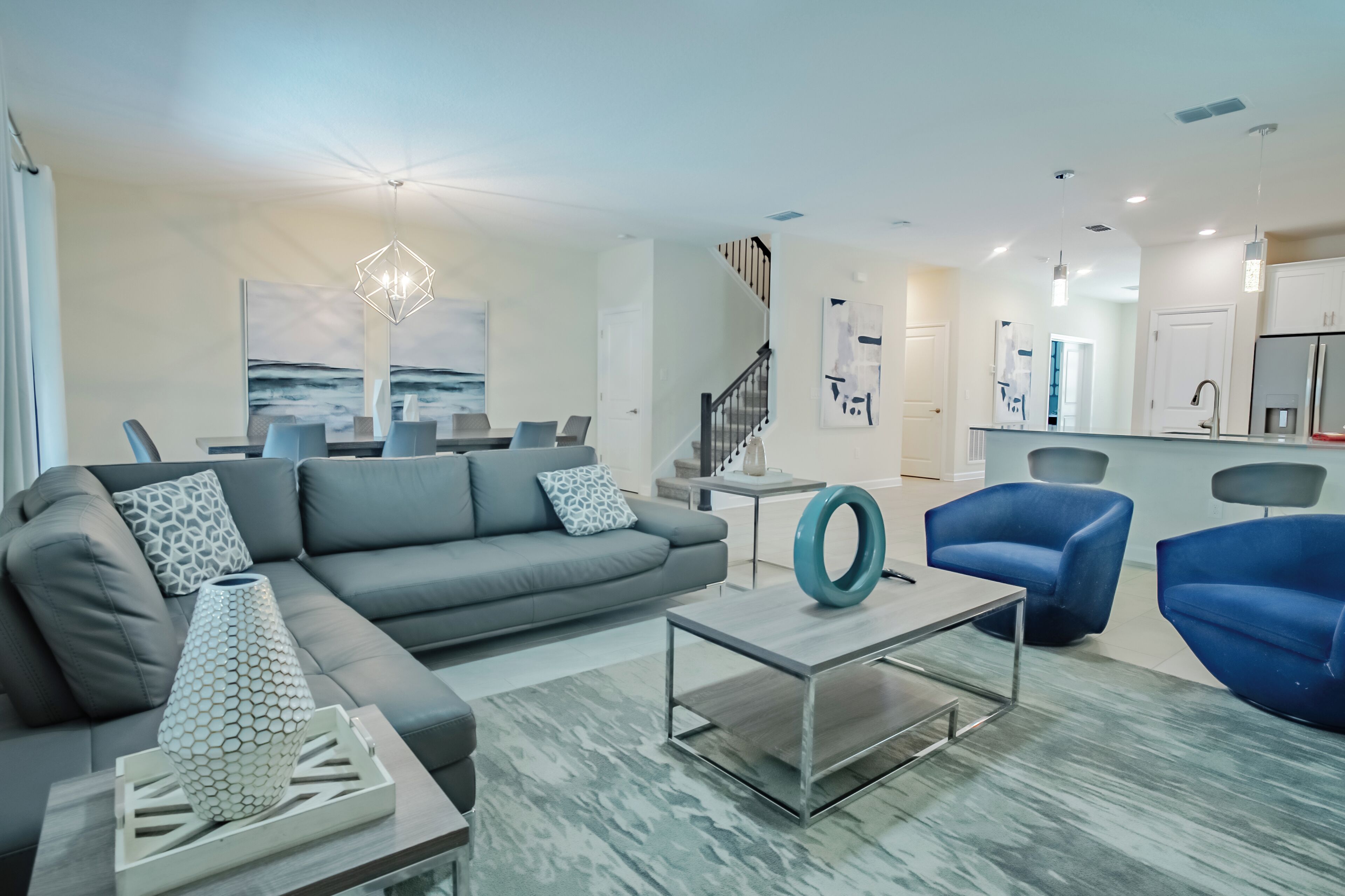 A modern living room with a grey sofa, blue armchairs, a coffee table, and a dining area with a white table and chairs.