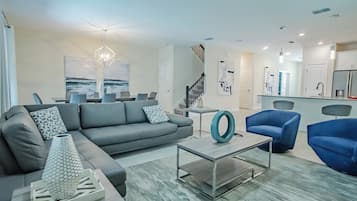 A modern living room with a grey sofa, blue armchairs, a coffee table, and a dining area with a white table and chairs.