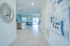 A spacious hallway with a modern kitchen in the background, a large abstract painting on the right wall, and a decorative mirror on the left. - 9BR Disney Villa Near Disney, Private Pool, Game Room, Sleeps 20+ (Kissimmee)