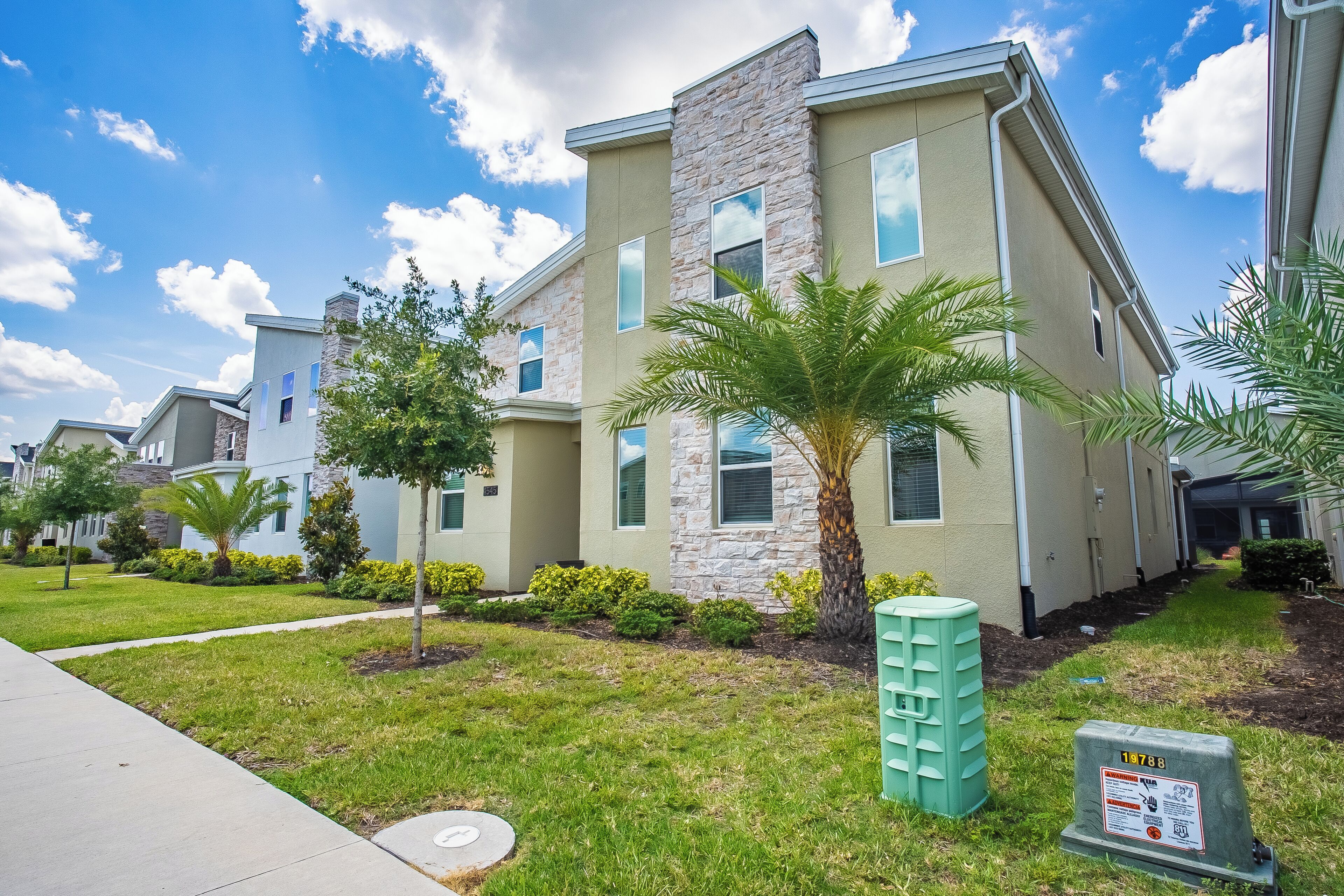 A modern apartment building with a stone facade, multiple windows, and a well-maintained lawn with palm trees.