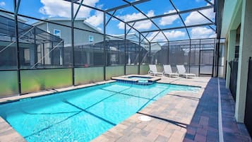 An indoor swimming pool with a clear view of the sky through a glass enclosure, surrounded by a brick patio and lounge chairs.
