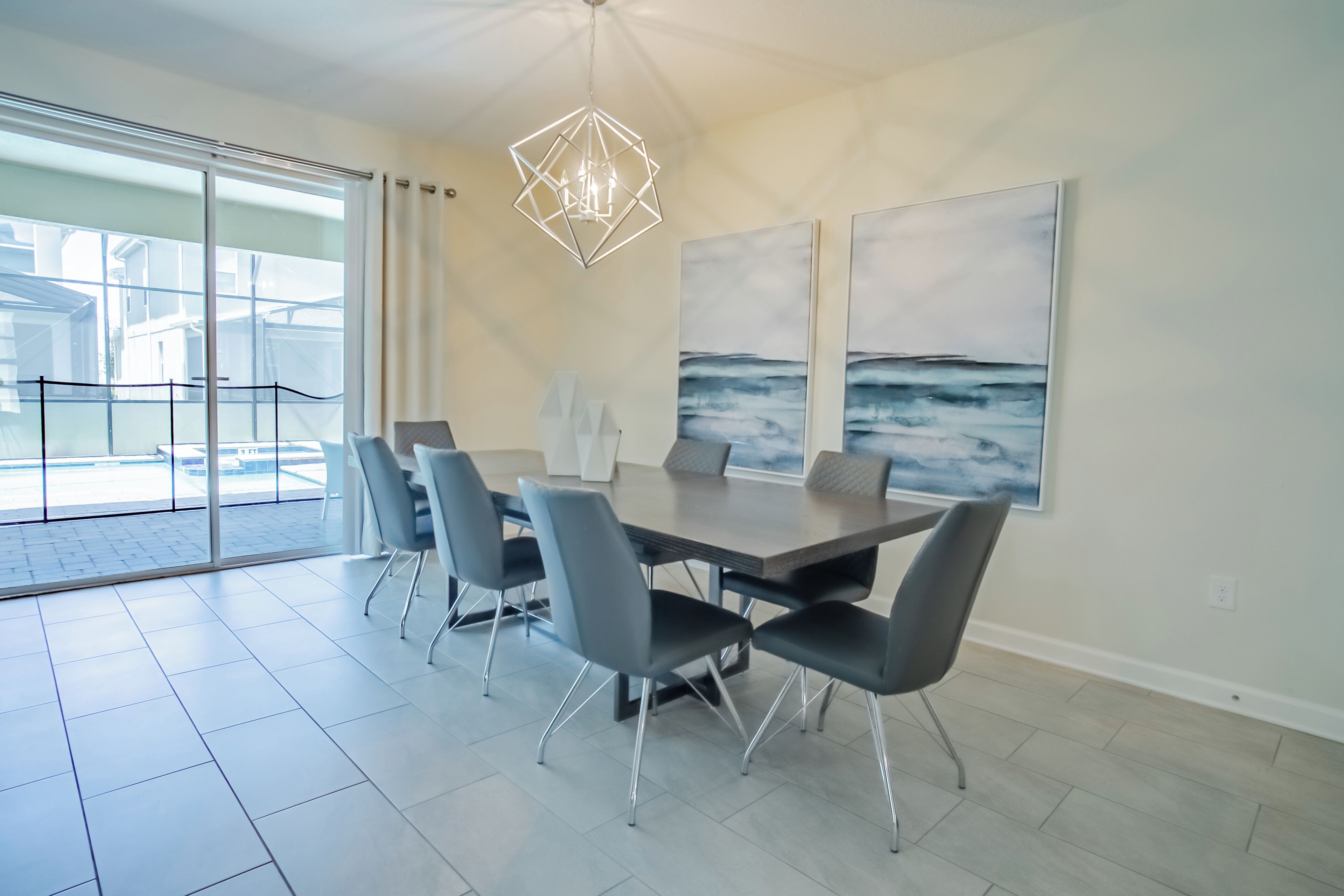 A modern dining area with a large table, six chairs, and a geometric pendant light.