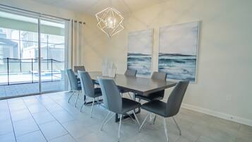 A modern dining area with a large table, six chairs, and a geometric pendant light.