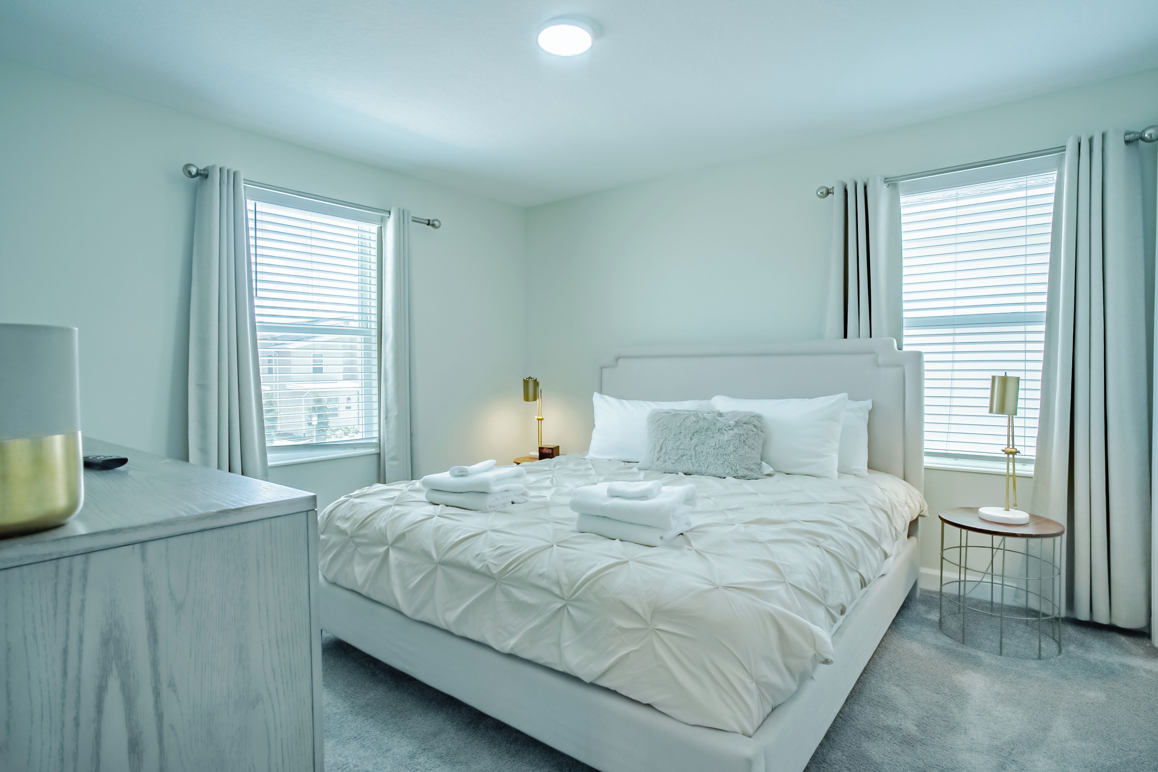 A modern bedroom with a large bed, bedside tables, and a view of the city through the windows.