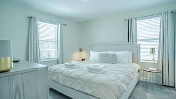 A modern bedroom with a large bed, bedside tables, and a view of the city through the windows.