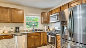 A kitchen with wooden cabinets, stainless steel appliances, a dishwasher, and a window with a view of greenery. - Fenced Yard! Family Home, 14 Mi to DC Sites (Lanham)