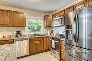 A kitchen with wooden cabinets, stainless steel appliances, a dishwasher, and a window with a view of greenery. - Fenced Yard! Family Home, 14 Mi to DC Sites (Lanham)
