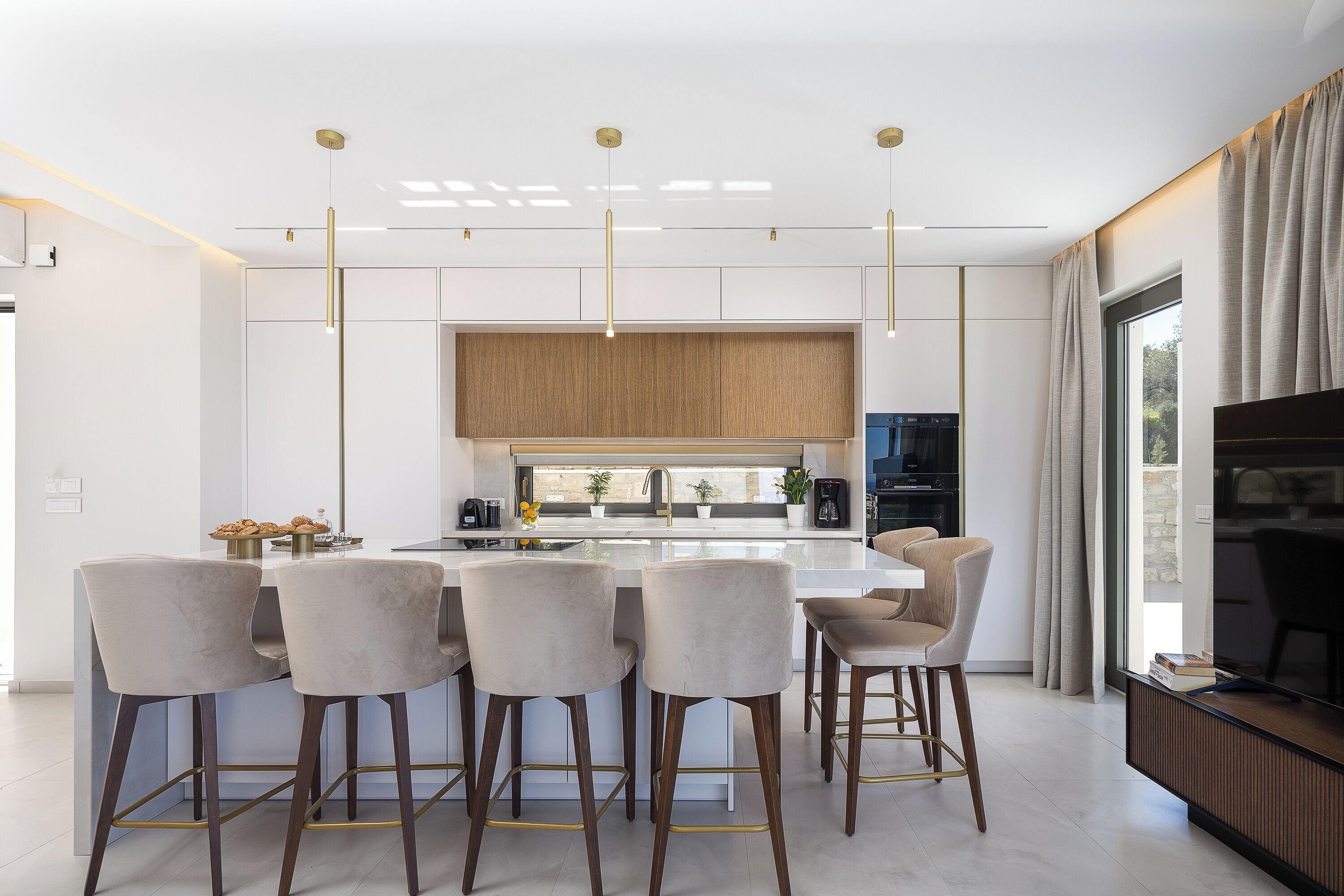 A modern kitchen with a central island, bar stools, pendant lighting, and a view of the outdoors.