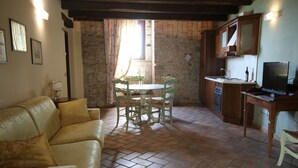 A living room with a sofa, a dining table with chairs, a kitchen area with cabinets and a TV, and a brick wall. - Residence in Monteprandone with 2 bedrooms sleeps 6 (Monteprandone)