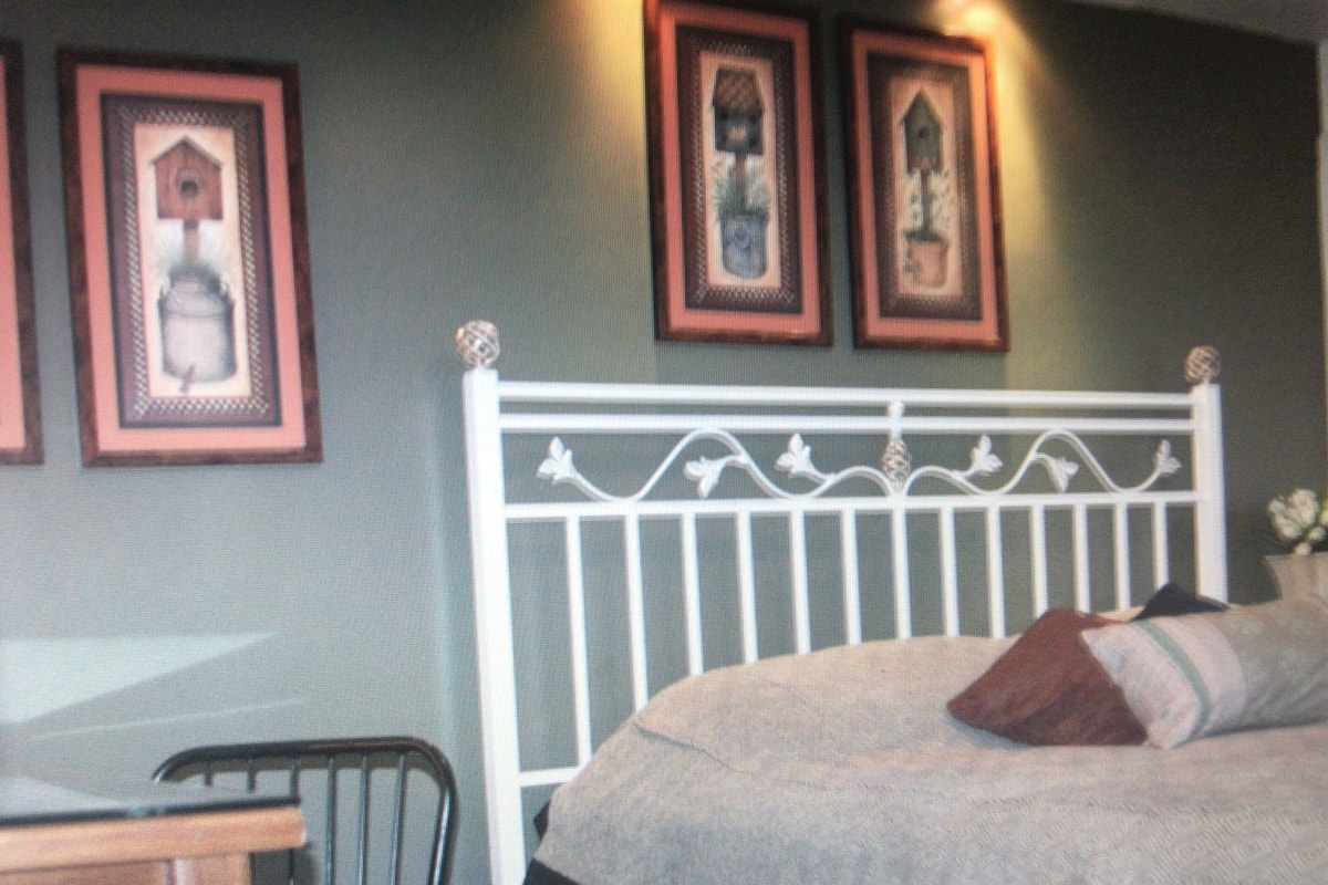 A bedroom with a white metal headboard, a bed with a beige cover, and three framed pictures on the wall.
