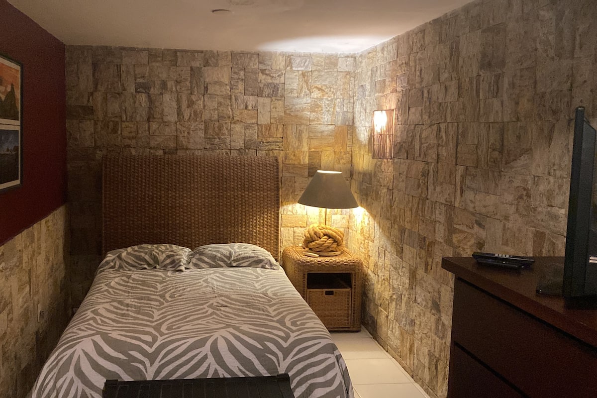 A bedroom with a stone wall, a bed with zebra-patterned bedding, a lamp, and a small wooden nightstand.