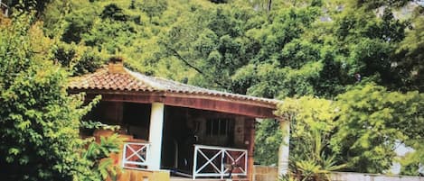 Uma casa pequena com telhado de telhas, varanda e um banco.