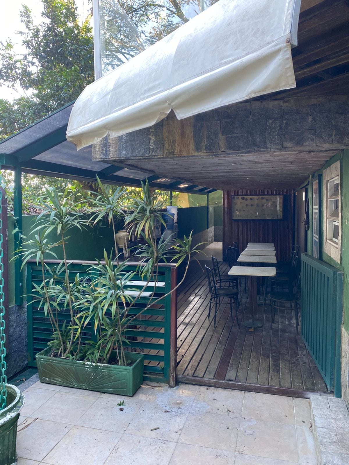 Un espace extérieur abrité, aménagé avec des tables et des chaises, et entouré de plantes en pot.