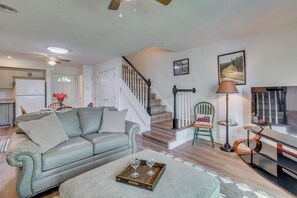 Un salon avec un canapé, une table basse sur laquelle se trouvent des verres, un escalier et, au fond, une cuisine.