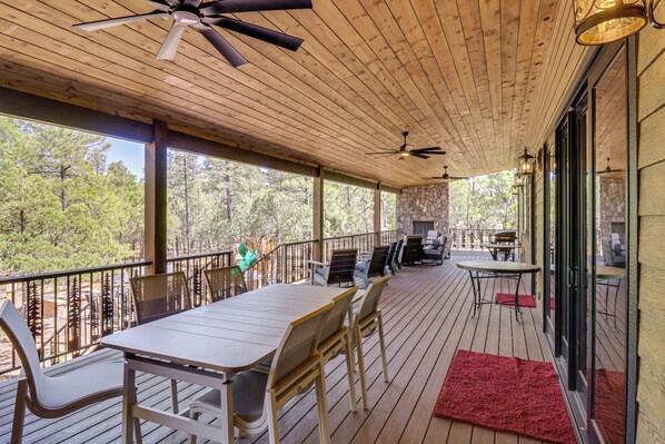 A covered outdoor deck with a table and chairs, a ceiling fan, and a stone fireplace. - Spacious Family Gem w/ Patio, 3 Mi to Rainbow Lake (Lakeside)