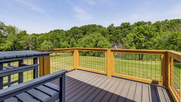 A wooden deck with a metal railing overlooking a grassy area with trees. - Smoky Mountain Riverfront Barndominium (Kodak)