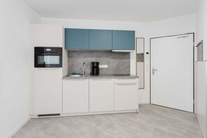 A compact kitchen with white cabinets, a black oven, a coffee maker, and a teal upper cabinet.