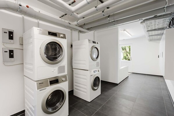 A modern laundry facility with stacked washers and dryers, a control panel, and a view of the outdoors.