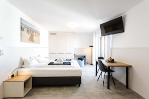 Ein Hotelzimmer mit Bett, Nachttisch, Schreibtisch, Stuhl, Fernseher und einem Bild an der Wand.