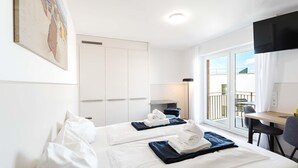 A hotel room with two beds, a desk, a chair, a TV, and a balcony with a view.