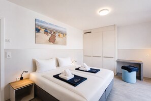 A hotel room with a bed, bedside tables, a painting, a wardrobe, and a small seating area.