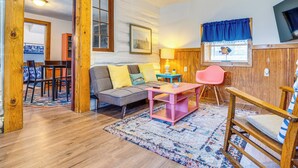 A cozy living room with a sofa, a pink table, a wooden chair, a rug, and a window with a blue curtain. - Family Home in Monticello! Water-View Retreat (Monticello)