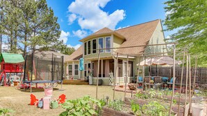 Une maison à deux étages avec un patio couvert, une cour arrière clôturée et un trampoline.