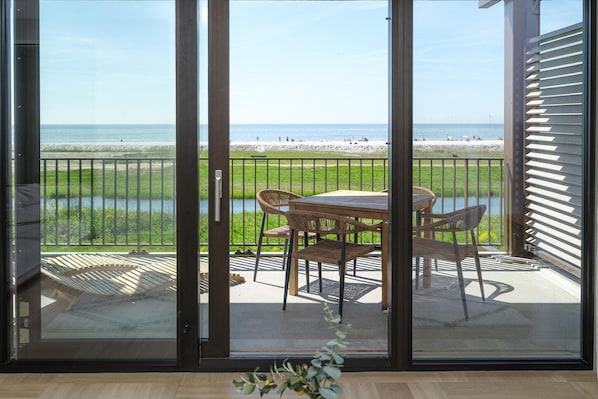 A balcony with a table and chairs, a view of the beach, and a railing.
