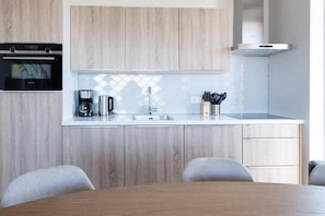 Une cuisine moderne avec des meubles en bois, un four encastré, une machine à café et un évier.