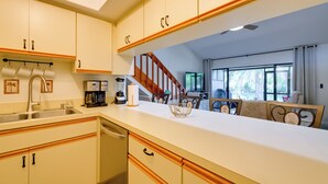 Una cocina con armarios de madera, una cafetera y un comedor con sillas.