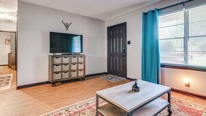 Une pièce avec un téléviseur posé sur un chariot en bois, une porte, une fenêtre avec des rideaux et un tapis à motifs.