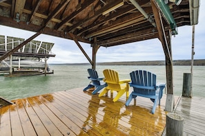 Une terrasse en bois avec trois chaises Adirondack, un espace abrité et une vue sur l’eau.
