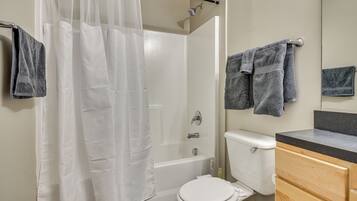 A bathroom with a bathtub, toilet, and wooden vanity.