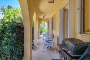 Eine überdachte Terrasse im Freien mit Grill, Stühlen und Blick ins Grüne.