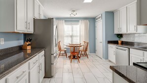 Une cuisine moderne avec des meubles blancs, un plan de travail en granit, un réfrigérateur en acier inoxydable et une table à manger avec des chaises.