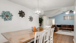 Un espace repas comprenant une table en bois, des chaises blanches, un lustre et un ventilateur de plafond.