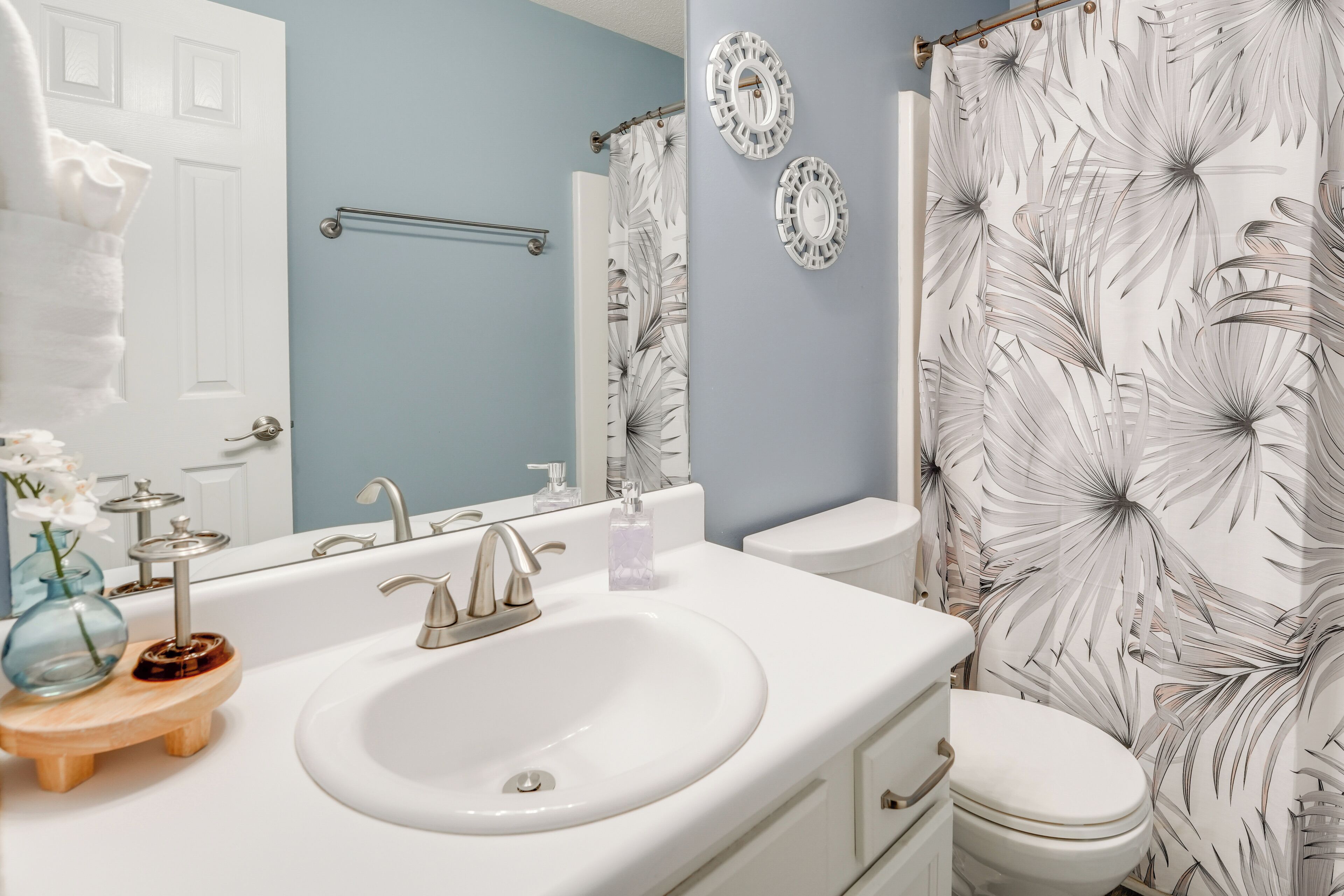A bathroom with a white sink, a toilet, a shower curtain with a floral pattern, and a towel rack.