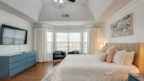 Une chambre à coucher avec un grand lit, un téléviseur à écran plat, une commode bleue et une fenêtre avec des rideaux.