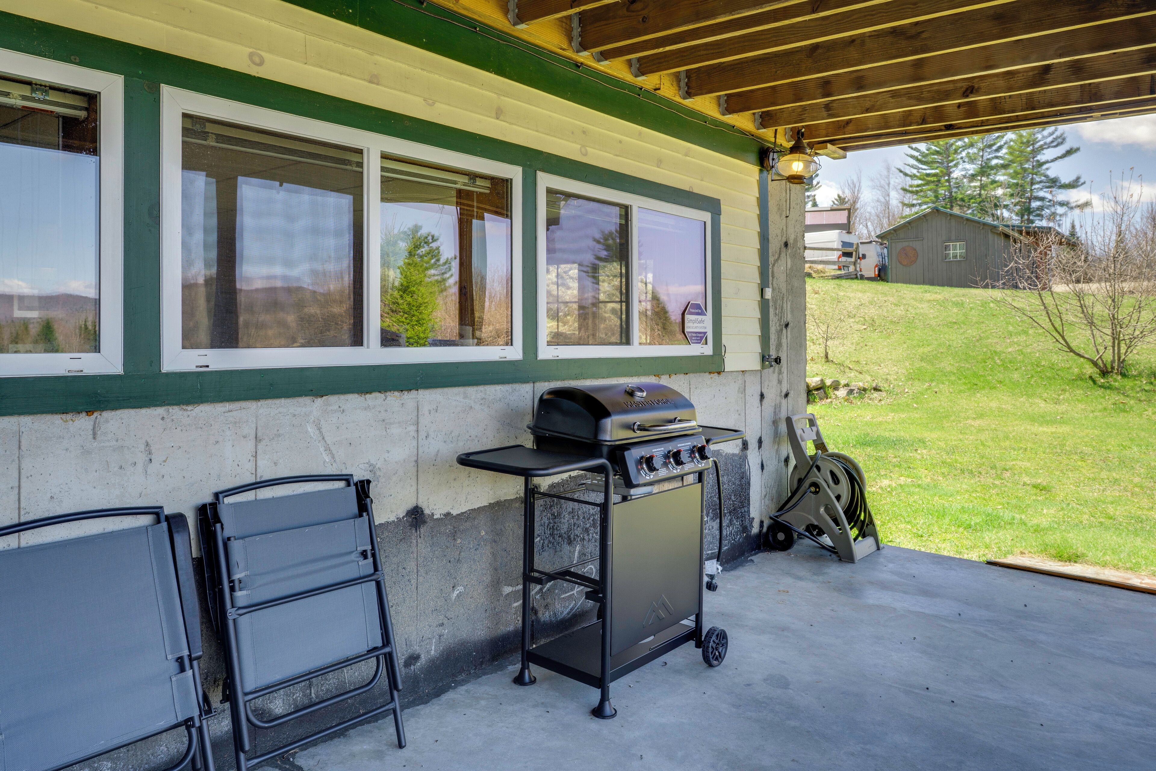 An outdoor patio with a grill, a cart, and a view of a house and trees.