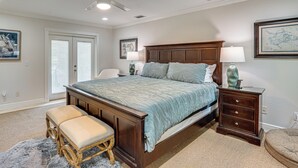 Een slaapkamer met een bed, nachtkastje, bankje, plafondventilator en een deur.