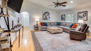 Een woonkamer met een hoekbank, een bruine leren fauteuil, een plafondventilator en kunstwerken aan de muur.