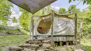 Una cama rústica al aire libre con dosel, rodeada de rocas y follaje.