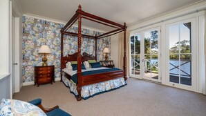A four-poster bed with a canopy, a wooden nightstand with a lamp, and a view of a body of water through large sliding glass doors. - Chalet Deux at Woodman Estate (Moorooduc)