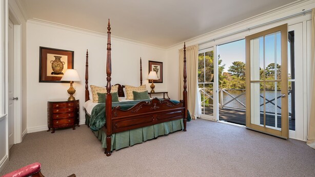 A four-poster bed with a green bedspread, two bedside tables with lamps, and a view of a lake through a sliding glass door.