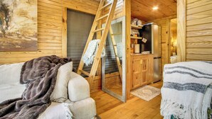 A cozy cabin interior with a wooden interior, a ladder leading to a loft, a refrigerator, and a bed with a blanket. - Tiny Cabin Getaway in the Tennessee River Valley (Rogersville)