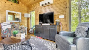 A wooden cabin interior with a sofa, a television, a cabinet, and a large window. - Tiny Cabin Getaway in the Tennessee River Valley (Rogersville)