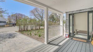 A covered porch with a bench, a door leading to a room, and a view of a street with trees and a building. - 2 Mi to Nantasket Beach! Group Retreat w/ Patio (Hull)
