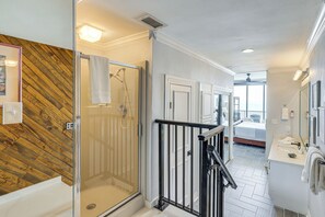 Ein modernes Badezimmer mit Duschkabine aus Glas, einer Wand mit Holzverkleidung, einem schwarzen Metallgeländer und einem weißen Waschbecken.